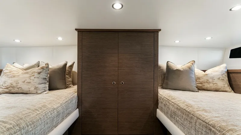 Slide: The Image of Twin Guest Stateroom with Storage - Valhalla 55 Sport Yacht This elegant twin guest stateroom features plush bedding and ample natural light, creating a cozy retreat for guests. The central wooden cabinet provides generous storage space, complementing the sleek, modern design. Recessed lighting enhances the warm a - 6332938