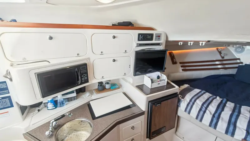 Slide: The Image of 2006 Grady-White 330 Express - "POLE POSITION": Galley and Cabin Area This image showcases the well-equipped galley and cozy cabin area of the 2006 Grady-White 330 Express. The galley features a compact sink, microwave, and ample storage, ideal for preparing meals while on the water. Adjacent to the galley, the cabin offers - 6572957