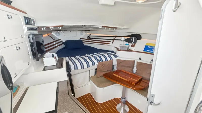 Slide: The Image of 2006 Grady-White 330 Express - "POLE POSITION": Interior Cabin with Dinette and Berth This inviting cabin of the 2006 Grady-White 330 Express features a cozy berth with striped bedding and plush cushions, offering a comfortable retreat. The adjacent dinette area includes a convertible table and cushioned seating, ideal for dining or relaxa - 6572953