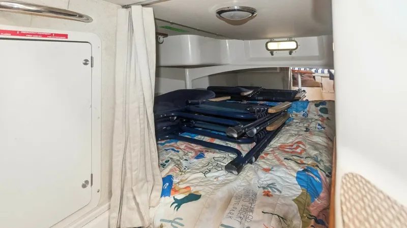 Slide: The Image of 2006 Grady-White 330 Express - "POLE POSITION": Cozy Cabin Berth with Storage This inviting cabin berth on the 2006 Grady-White 330 Express offers a comfortable sleeping area adorned with a colorful quilt. Above the berth, practical storage space is utilized for stowing foldable chairs, maximizing functionality. The soft lighting a - 6572962