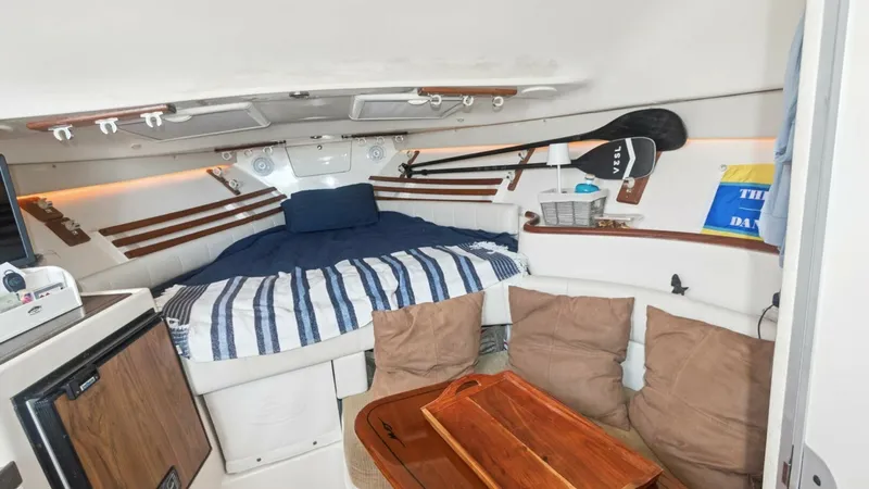 Slide: The Image of 2006 Grady-White 330 Express - "POLE POSITION": Cozy Forward Cabin with Dinette This inviting forward cabin on the 2006 Grady-White 330 Express features a comfortable V-berth with plush cushions and striped bedding. The space is enhanced by ambient lighting and practical storage solutions, including overhead compartments. A compact d - 6572958
