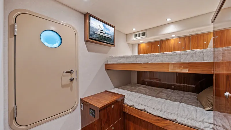 Slide: The Image of Cozy Guest Stateroom with Bunk Beds This inviting guest stateroom features comfortable bunk beds with plush bedding, perfect for accommodating additional guests. The rich wood finishes and soft, ambient lighting create a warm and welcoming atmosphere. A small porthole and tasteful nautical - 7377924