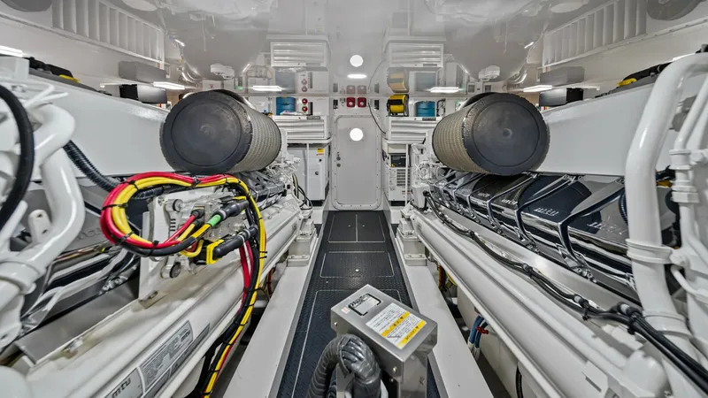 Slide: The Image of Engine Room with Twin Engines This image showcases the immaculate engine room of the 2021 Viking 72 Enclosed Bridge. The space is equipped with twin engines, highlighted by their sleek, efficient layout and advanced engineering. Bright overhead lighting and well-organized cable manage - 7377934
