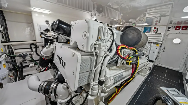 Slide: The Image of Engine Room with MTU Engines The image showcases the pristine engine room of the 2021 Viking 72 Enclosed Bridge, featuring powerful MTU engines. The space is meticulously organized, accentuated by clean, white surfaces and neatly arranged wiring, reflecting high-quality engineering a - 7377931