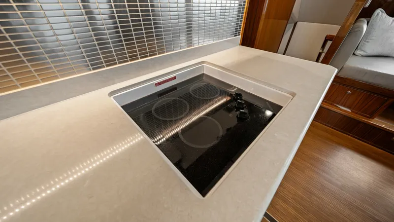 Slide: The Image of Galley Induction Cooktop and Counter This image showcases the sleek induction cooktop set within a polished countertop in the Viking 72 Enclosed Bridge. The sophisticated tile backsplash adds a modern touch while providing easy maintenance. The surrounding cabinetry offers ample storage, enh - 7377897