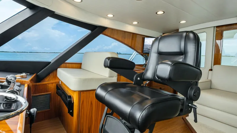 Slide: The Image of Enclosed Bridge Helm Station The enclosed bridge of the Viking 72 features a state-of-the-art helm station with a luxurious black leather captain's chair. The space is surrounded by expansive windows offering panoramic views, enhancing navigation and comfort. Rich wood finishes and r - 7377885