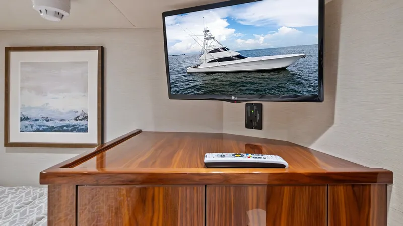 Slide: The Image of Stateroom Entertainment and Storage Unit This image showcases a sleek entertainment setup within the stateroom of the 2021 Viking 72 Enclosed Bridge. A wall-mounted flat-screen TV is positioned above a finely crafted wooden storage unit, offering both functionality and elegance. The warm wood to - 7377914