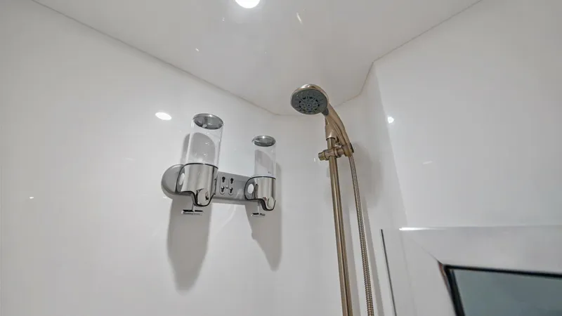 Slide: The Image of Luxurious Enclosed Shower Detail This image showcases the sleek, modern shower area of the 2021 Viking 72 Enclosed Bridge. Featuring a stylish chrome handheld showerhead and built-in dispenser, the space is designed for both functionality and luxury. The high-gloss white surfaces and rec - 7377916