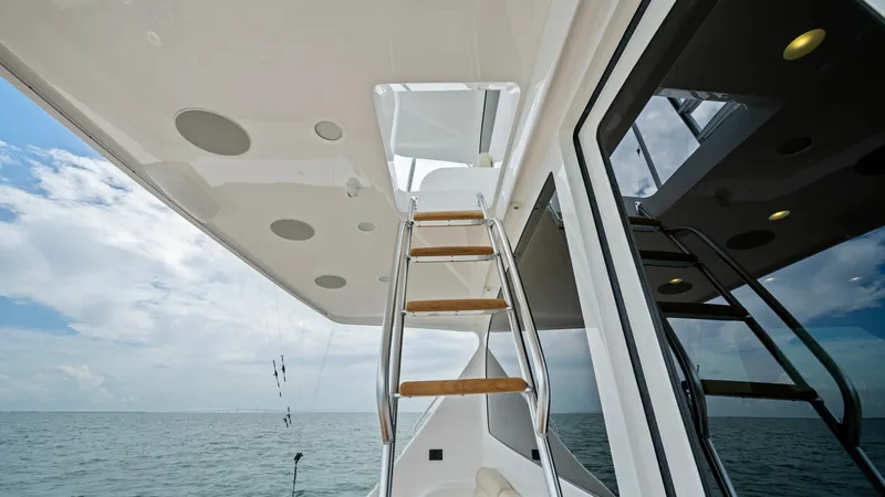 Slide: The Image of Flybridge Access Ladder View This image showcases the sleek access ladder to the flybridge of the 2021 Viking 72 Enclosed Bridge. The ladder features polished stainless steel handrails and teak steps, offering both style and safety. The substantial overhang provides shade and include - 7377940