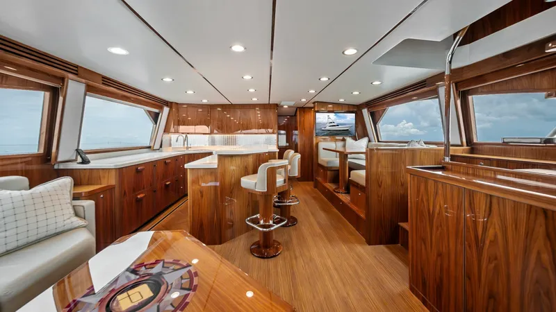 Slide: The Image of Spacious Salon and Helm Area This elegant salon of the 2021 Viking 72 Enclosed Bridge features luxurious wood finishes and expansive windows, offering panoramic ocean views. The area is equipped with plush seating and a stylish helm, ensuring comfort and functionality. The ambient li - 7377893
