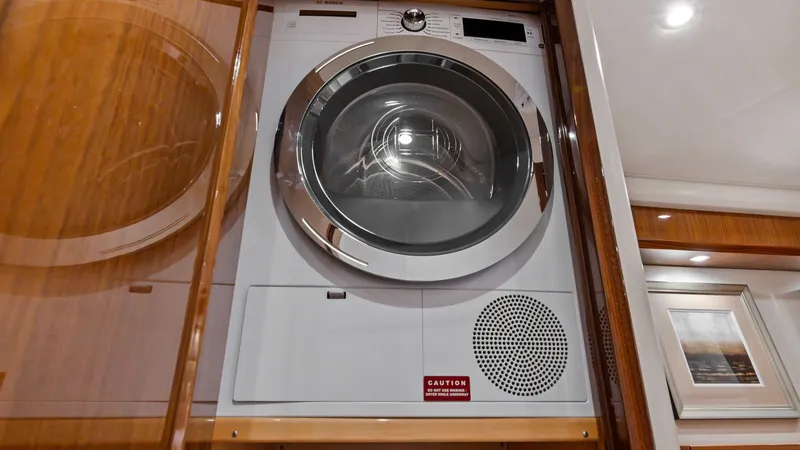 Slide: The Image of Laundry Area with Washer/Dryer Unit This modern laundry area on the Viking 72 Enclosed Bridge features a sleek, built-in washer and dryer unit. The high-gloss wooden cabinetry provides a sophisticated touch, seamlessly integrating the appliance into the yacht's interior. The space is well-l - 7377912