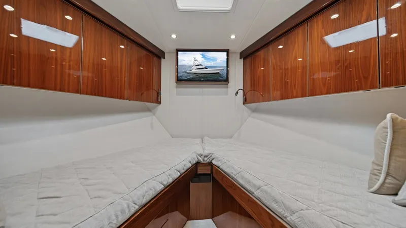 Slide: The Image of Luxurious Twin Guest Cabin This inviting twin guest cabin on the Viking 72 Enclosed Bridge features sleek, high-gloss wooden cabinetry providing ample storage. The comfortable twin berths are elegantly designed with plush bedding, creating a cozy yet stylish atmosphere. A mounted f - 7377917