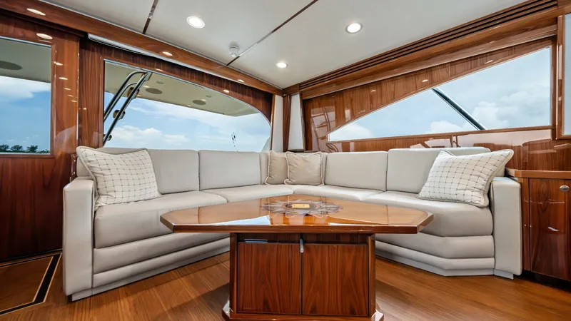 Slide: The Image of Luxurious Salon Seating Area The salon of the 2021 Viking 72 Enclosed Bridge showcases an elegant and spacious seating area with a plush L-shaped sofa. The high-gloss wood finishes and large windows create a warm, inviting atmosphere with ample natural light. A stylish wooden coffee - 7377892