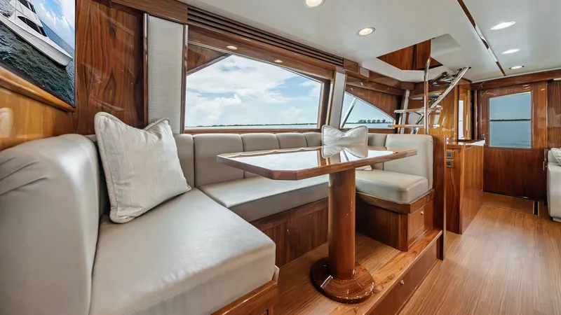 Slide: The Image of Main Deck Dining Area The main deck dining area of the 2021 Viking 72 Enclosed Bridge features elegant wood finishes and expansive windows for stunning views. The plush L-shaped seating provides comfort, complemented by a polished wood dining table. Overhead recessed lighting - 7377900