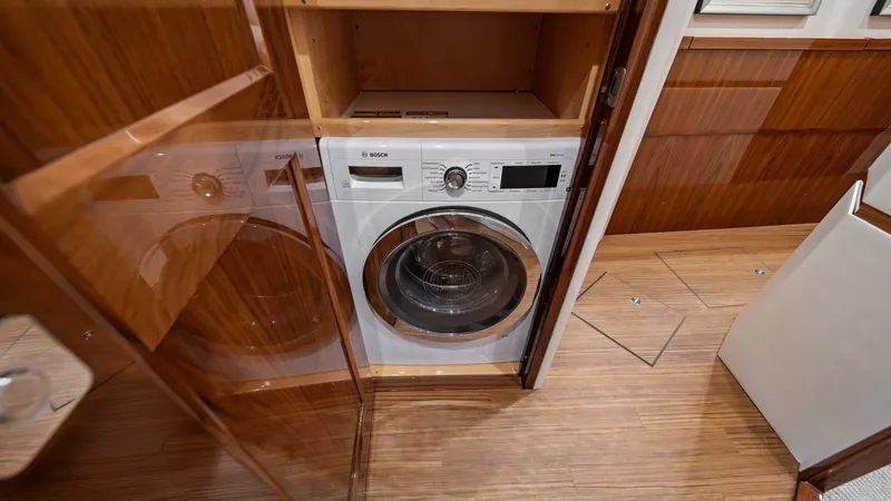 Slide: The Image of Laundry Area with Washer/Dryer Unit This image showcases the compact and efficient laundry area on the Viking 72 Enclosed Bridge. The Bosch washer/dryer unit is neatly integrated into the wooden cabinetry, ensuring functionality without compromising on style. The high-gloss wood finishes an - 7377911