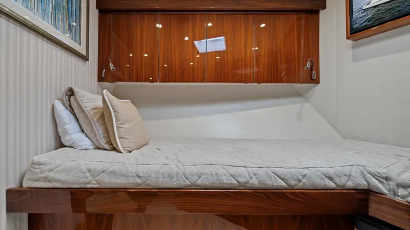 Slide: The Image of Guest Stateroom with Upper Cabinetry This cozy guest stateroom on the Viking 72 Enclosed Bridge features a comfortable single berth with plush bedding. The elegant wooden cabinetry above provides ample storage, complementing the room's sophisticated design. Soft lighting and tasteful artwork - 7377918