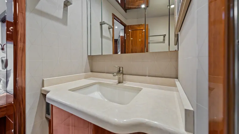Slide: The Image of Elegant Bathroom Vanity Area This sophisticated bathroom vanity features a sleek, integrated sink set in a polished countertop, complemented by rich wood cabinetry. The mirrored cabinet above provides ample storage and enhances the room's spacious feel. Modern fixtures and a subtle g - 7377922