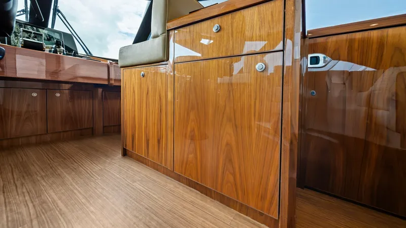 Slide: The Image of Enclosed Bridge Helm Cabinetry This image showcases the exquisite wood cabinetry in the enclosed bridge of the 2021 Viking 72 Enclosed Bridge. The high-gloss finish highlights the rich grain of the wood, adding a touch of elegance and sophistication. The cabinetry is designed for funct - 7377887
