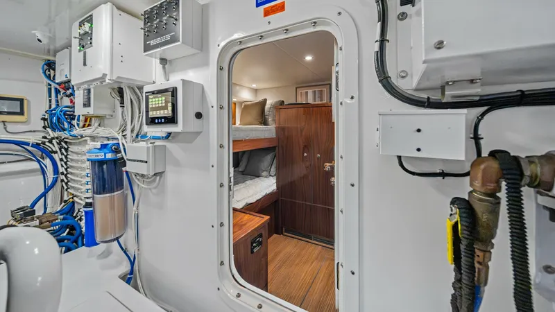Slide: The Image of Engine Room Access to Crew Quarters This image showcases the entrance to the crew quarters from the engine room of the 2021 Viking 72 Enclosed Bridge. The doorway leads to a cozy bunk area with neatly arranged bedding and warm wood finishes, providing a comfortable resting space for the cre - 7377928