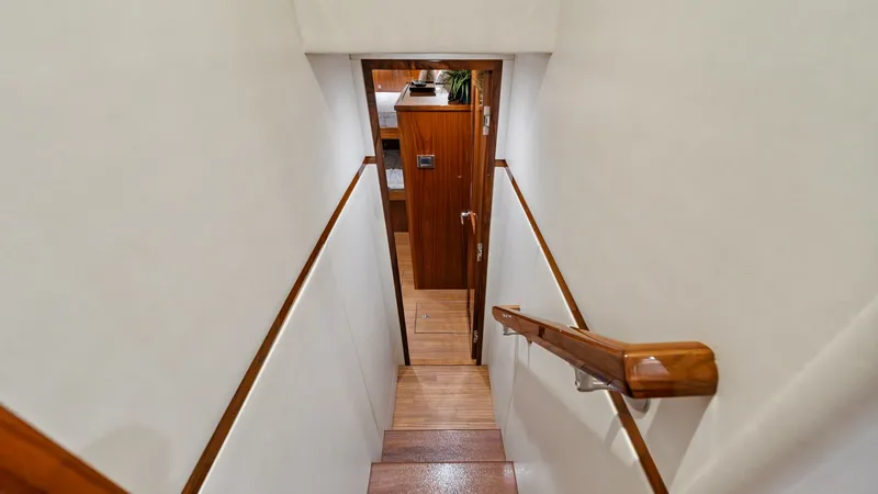 Slide: The Image of Interior Stairway to Lower Deck This image showcases the elegant stairway leading to the lower deck of the Viking 72 Enclosed Bridge. The staircase features polished wooden steps and handrails, complemented by sleek white walls, creating a warm and inviting transition between decks. The - 7377904