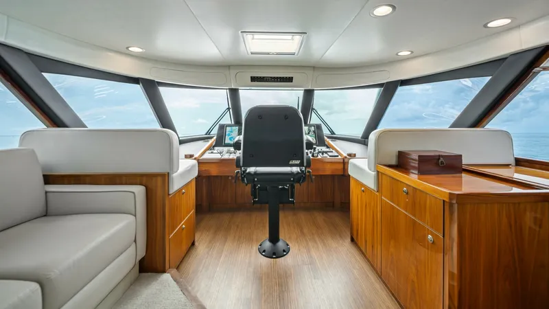 Slide: The Image of Enclosed Bridge Helm Station This enclosed bridge helm station of the Viking 72 offers panoramic views through expansive windows, ensuring optimal visibility while navigating. The central captain's chair is flanked by luxurious wood cabinetry and plush seating, combining functionalit - 7377877