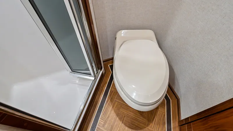 Slide: The Image of Luxury En-Suite Bathroom This elegant en-suite bathroom on the 2021 Viking 72 Enclosed Bridge features a sleek, modern toilet and a spacious, glass-enclosed shower. The high-quality wood flooring and polished finishes add a touch of luxury and sophistication, making this a comfor - 7377927
