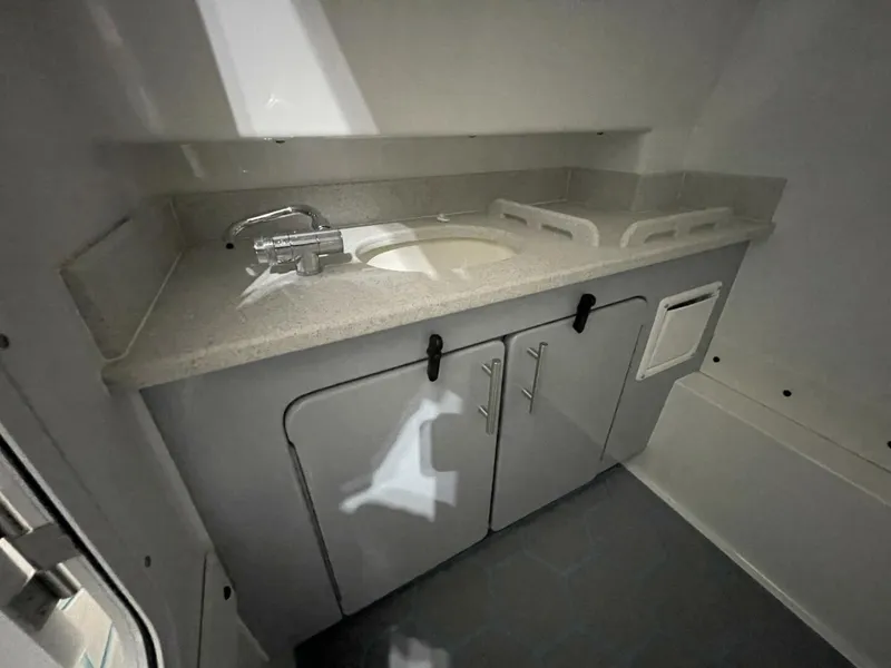 Slide: The Image of Boat Head Sink and Cabinetry Inside Center Console Compartment Close-up of molded sink, faucet, countertop, and under-cabinet storage. Functional head compartment ideal for offshore cruising and long fishing trips. - 5799732
