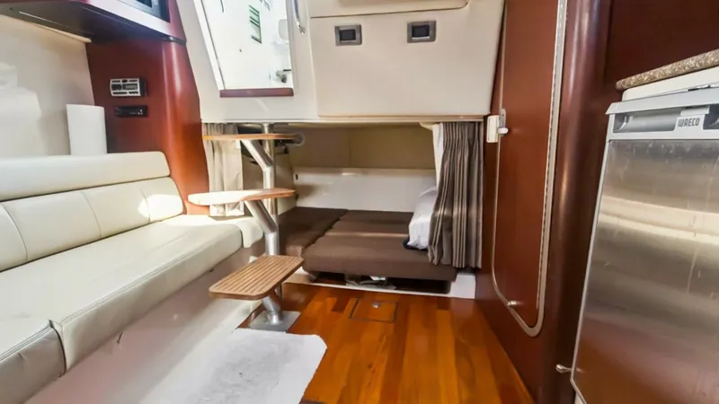 Slide: The Image of Interior Cabin with Convertible Seating The interior cabin of the 2008 Boston Whaler 34 Outrage showcases a versatile space with convertible seating and a cozy sleeping area. The warm wood flooring complements the sleek, modern design, while ample natural light filters through the cabin window. - 7672497