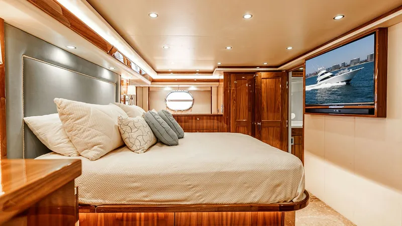 Slide: The Image of Luxurious Master Stateroom The master stateroom on the Viking 80 Skybridge exudes elegance with its rich wood finishes and sophisticated lighting. A plush king-size bed is the centerpiece, complemented by ample storage and a flat-screen TV for entertainment. The porthole adds a nau - 6478717