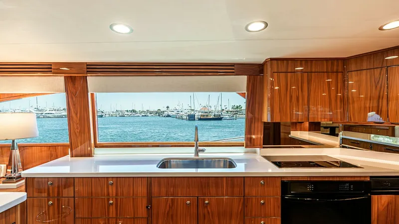 Slide: The Image of Galley with Ocean View The galley of the Viking 80 Skybridge features sleek, polished wood cabinetry and modern appliances, offering both functionality and style. A large window above the sink provides a stunning view of the surrounding marina, enhancing the sense of openness a - 6478709