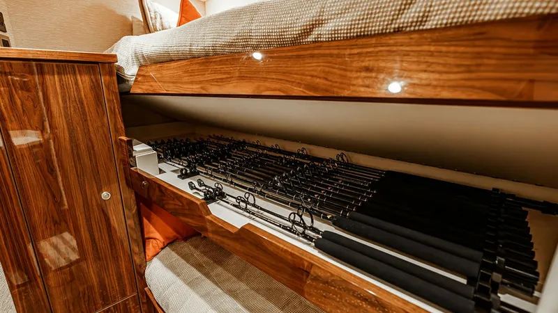 Slide: The Image of Guest Cabin with Fishing Rod Storage The guest cabin on the Viking 80 Skybridge features cozy bunk beds with integrated fishing rod storage beneath. The warm wood finishes and ambient lighting create a welcoming atmosphere, perfect for relaxation after a day on the water. This clever use of - 6478727