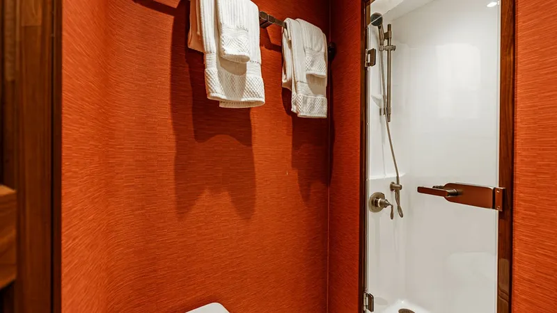 Slide: The Image of Elegant Guest Bathroom This guest bathroom features a sleek, modern design with vibrant red textured walls that add a touch of elegance. The space is equipped with a compact yet functional shower enclosed with a glass door, and a neatly arranged towel rack. High-quality fixture - 6478735