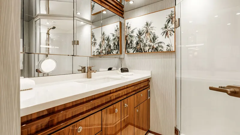 Slide: The Image of Elegant Yacht Bathroom with Shower This luxurious yacht bathroom features a sleek vanity with a polished countertop and stylish faucet, complemented by rich wood cabinetry. The mirrored walls and tropical artwork add a touch of sophistication and spaciousness. A modern glass-enclosed showe - 6478720