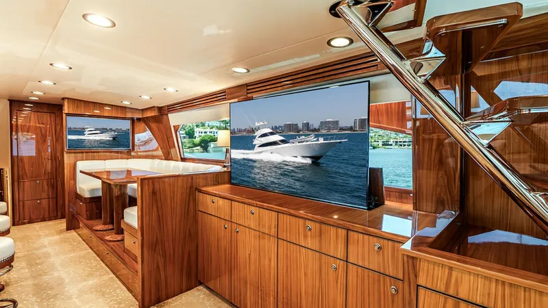 Slide: The Image of Luxurious Salon with Entertainment System This elegant salon aboard the 2019 Viking 80 Skybridge features rich wood cabinetry and modern design elements. A large flat-screen TV is prominently displayed, offering a state-of-the-art entertainment experience. The space is illuminated by recessed lig - 6478710