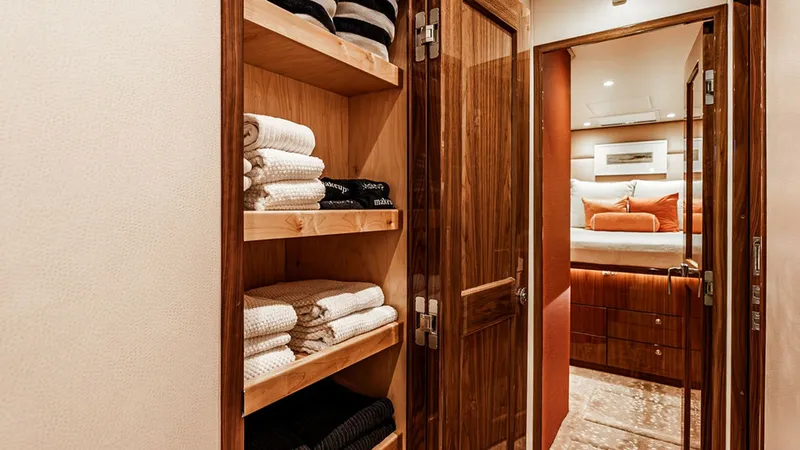 Slide: The Image of Luxury Linen Closet and Stateroom View This image showcases the elegant linen closet of the 2019 Viking 80 Skybridge, featuring rich wood finishes and ample shelving for towels and linens. Beyond the closet, a glimpse into the plush stateroom reveals a tastefully appointed space with soft ligh - 6478736