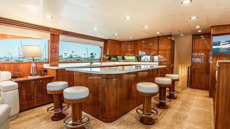 Slide: The Image of Luxurious Salon with Breakfast Bar This elegant salon on the Viking 80 Skybridge features a polished breakfast bar with plush, circular stools, perfect for casual dining or entertaining guests. The warm wood cabinetry and ambient lighting create a cozy yet sophisticated atmosphere. Large w - 6478702