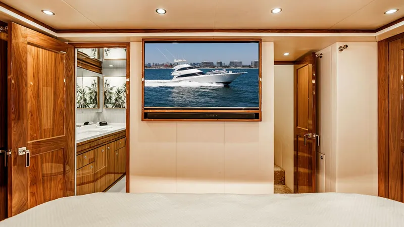 Slide: The Image of Master Stateroom with Ensuite This luxurious master stateroom boasts a large, comfortable bed with exquisite wood finishes. The space is enhanced by a flat-screen TV above sleek cabinetry, providing entertainment and ample storage. The ensuite bathroom, visible to the left, features m - 6478719