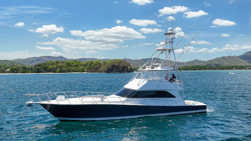 Slide: The Image of Side Profile of Viking 61 Convertible This image showcases the sleek side profile of the 2005 Viking 61 Convertible, 'Honey Girl'. The vessel's elegant lines and robust flybridge are complemented by its deep blue hull, creating a striking presence on the water. With its spacious deck and adva - 6449588