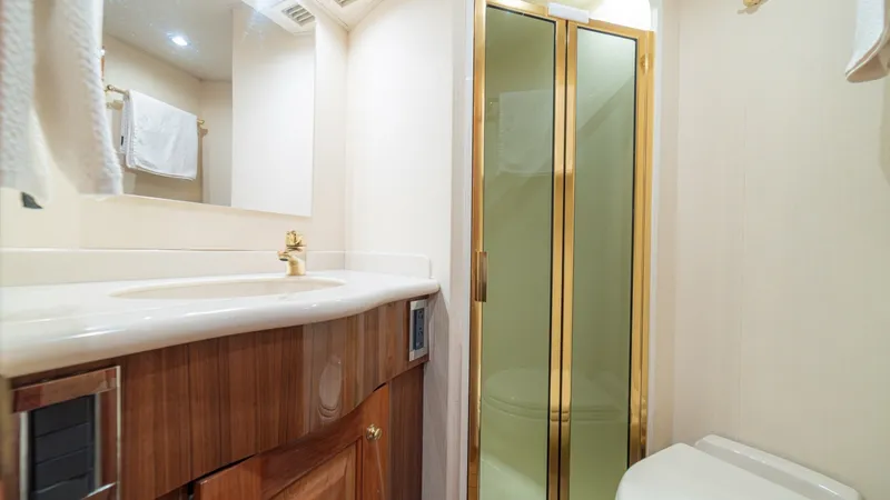 Slide: The Image of Luxurious Ensuite Bathroom This elegant ensuite bathroom on the 2005 Viking 61 Convertible features a sophisticated design with high-end finishes. The space is highlighted by a gleaming wood vanity topped with a seamless countertop and a gold-tone faucet. The shower boasts sleek gl - 6449547
