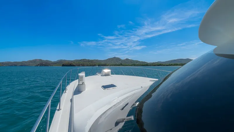 Slide: The Image of Bow View with Scenic Horizon The bow of the 2005 Viking 61 Convertible, 'Honey Girl', showcases a sleek design with clean lines and a spacious foredeck. The image highlights the vessel cruising under clear blue skies, offering panoramic views of the surrounding waters and distant lan - 6449577