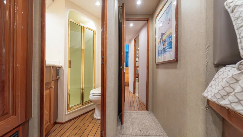 Slide: The Image of Hallway with Guest Head Access This image showcases the well-designed hallway of the 2005 Viking 61 Convertible, featuring access to a spacious guest head. The head includes a glass-enclosed shower and elegant wood cabinetry, enhancing the vessel's luxury. The teak and holly flooring a - 6449542