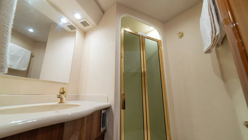 Slide: The Image of Elegant En-Suite Bathroom with Shower This luxurious en-suite bathroom features a sleek, enclosed shower with gold-trimmed glass doors, adding a touch of elegance to the space. The vanity is equipped with a stylish brass faucet and ample counter space, complemented by warm wooden cabinetry. R - 6449549