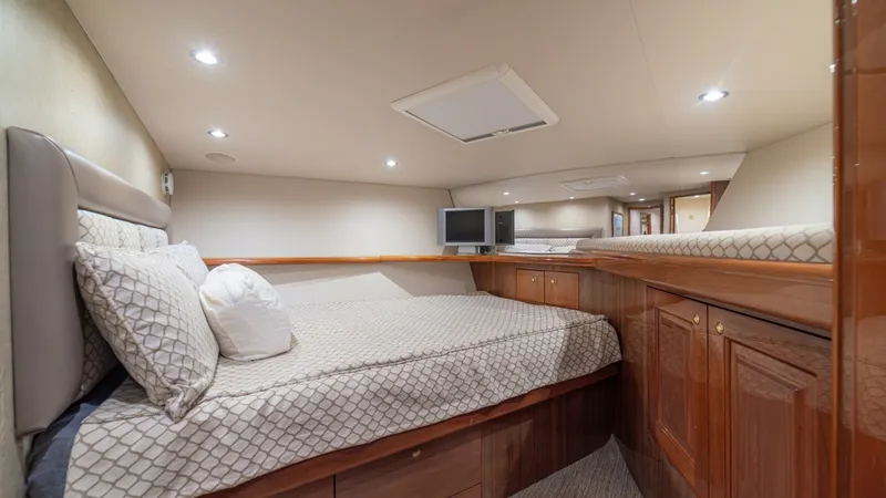 Slide: The Image of Spacious Forward Stateroom with Storage The forward stateroom on the Viking 61 Convertible 'Honey Girl' offers a plush, queen-sized berth adorned with elegant patterned bedding. Rich wood cabinetry provides ample storage, complemented by soft overhead lighting that enhances the cozy ambiance. A - 6449544