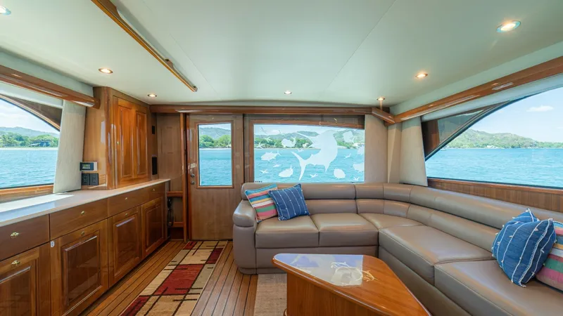 Slide: The Image of Spacious Salon with Panoramic Views The salon of the 2005 Viking 61 Convertible, Honey Girl, boasts expansive panoramic windows that flood the space with natural light and offer stunning sea views. The plush L-shaped sofa provides ample seating, complemented by a sleek wooden coffee table. - 6449521