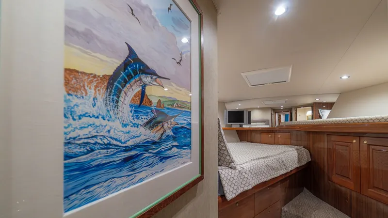 Slide: The Image of Guest Stateroom with Art Decor This inviting guest stateroom on the 2005 Viking 61 Convertible features a comfortable bed with elegant wood cabinetry, providing ample storage. The room is highlighted by a vibrant piece of artwork depicting a marlin, adding a splash of color and maritim - 6449543