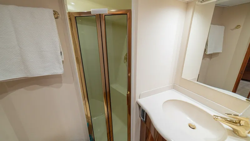 Slide: The Image of Elegant Yacht Bathroom with Shower This well-appointed bathroom on the 2005 Viking 61 Convertible features a sleek, enclosed shower with gold-toned trim that adds a touch of luxury. The vanity is equipped with a polished countertop and stylish fixtures, providing ample space for personal i - 6449527