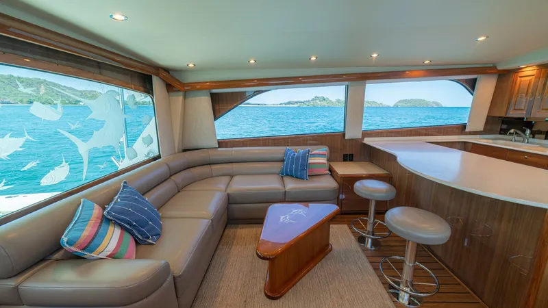 Slide: The Image of Spacious Salon with Panoramic Views The salon of the 2005 Viking 61 Convertible, 'Honey Girl', offers a blend of luxury and comfort with a plush L-shaped leather sofa and elegant wooden finishes. Large windows provide breathtaking panoramic views, creating a bright and airy atmosphere. The - 6449510