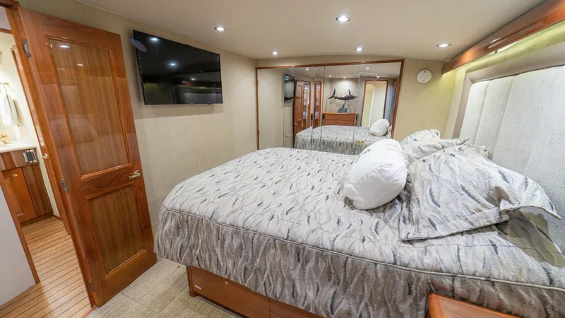 Slide: The Image of Master Stateroom with Ensuite Access This inviting master stateroom on the 2005 Viking 61 Convertible features a plush queen-sized bed with elegant bedding and ample storage beneath. The space is illuminated by recessed lighting, complementing the rich wood finishes and mirrored wall that en - 6449532