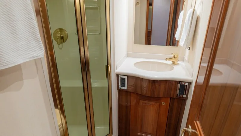 Slide: The Image of En-Suite Bathroom with Shower This elegant en-suite bathroom features a compact yet luxurious design with a glass-enclosed shower. Rich wood cabinetry complements the sleek white countertop, while gold-toned fixtures add a touch of sophistication. Ample lighting and a well-placed mirr - 6449529