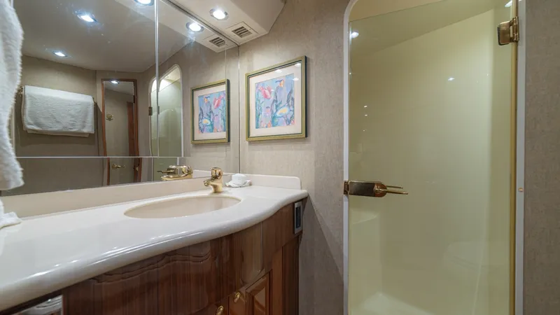 Slide: The Image of Elegant Yacht Bathroom with Shower This luxurious bathroom aboard the 2005 Viking 61 Convertible, 'Honey Girl', features a sleek vanity with a polished countertop and stylish gold accents. The space is well-lit with recessed lighting enhancing the modern decor, including tasteful wall art. - 6449539